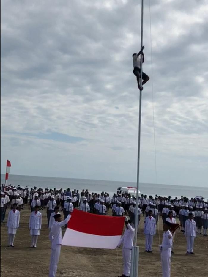 Joni memanjat tiang bendera untuk memperbaiki pengait yang bermasalah saat upacara HUT ke-73 RI. (Screenshot video viral) Joni memanjat tiang bendera untuk memperbaiki pengait yang bermasalah saat upacara HUT ke-73 RI. (Screenshot video viral)