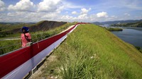 Seorang warga melintasi bendera Merah Putih yang dipasang di bukit Tungku Wiri atau Bukit Teletubies, Kampung Doyo Lama, Distrik Waibu, Kabupaten Jayapura, Papua, Senin (16/8/2021). ANTARA FOTO/Gusti Tanati  