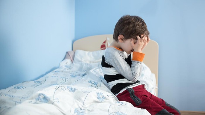 pelecehan anak Sad, upset little boy sitting on the edge of his bed. Covering his face with hands.