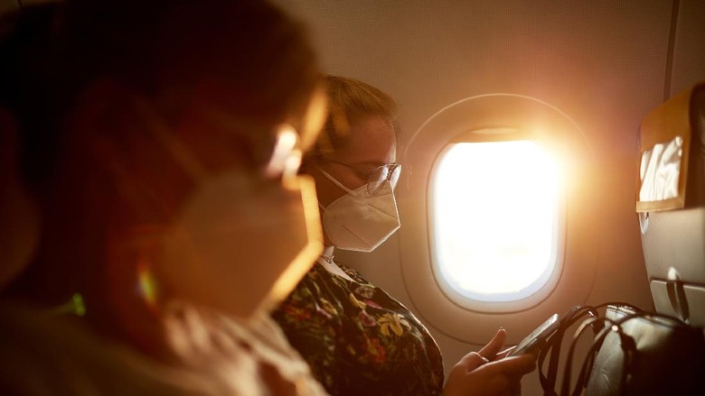 Side view with focus on background of mature Caucasian mother and teenage daughter wearing protective masks as they travel by airplane in time of COVID-19.