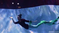 Seorang putri duyung tampak mengenakan kebaya saat berenang di dekat bendera Merah Putih berukuran raksasa yang dikibarkan di dalam air.