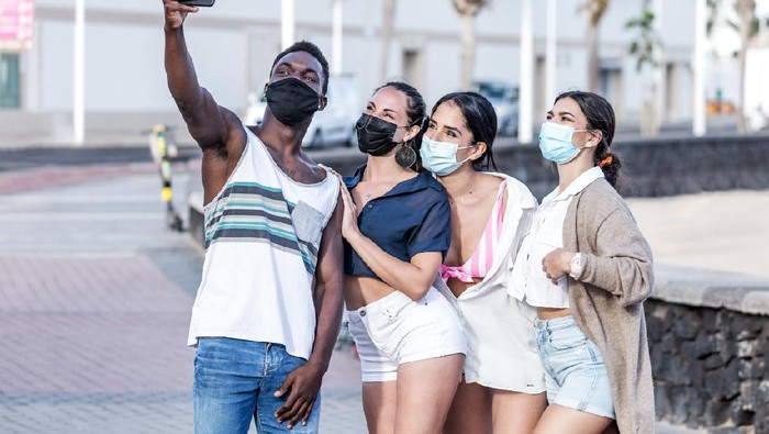 Group of smiling multiracial friends wearing masks standing in city and taking selfie on smartphone while spending time together in summer on Lanzarote
