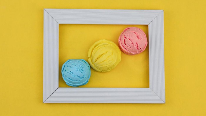 Homemade fruit ice cream in a white wooden frame on a yellow background, top view close-up.