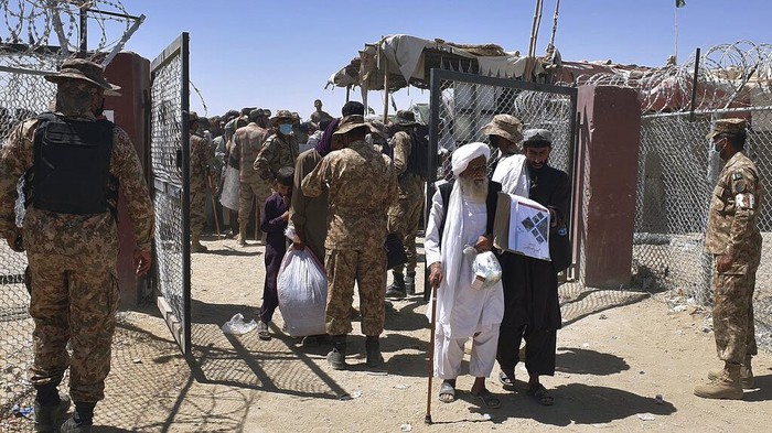 Pakistani soldiers stand guard while stranded people walk towards the Afghan side at a border crossing point, in Chaman, Pakistan, Friday, Aug. 13, 2021. Pakistan opened its Chaman border crossing for people who had been stranded in recent weeks. Juma Khan, the Pakistan border towns deputy commissioner, said the crossing was reopened following talks with the Taliban. (AP Photo/Jafar Khan)