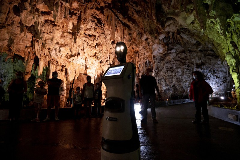 Persephone memandu para pengunjung di dalam gua Alistrati, sekitar 135 kilometer (84 mil) timur laut Thessaloniki, Yunani, Senin, 2 Agustus 2021. Persephone, yang disebut-sebut sebagai robot pertama di dunia yang digunakan sebagai pemandu wisata di dalam gua, telah menyambut pengunjung ke gua Alistrati, sejak pertengahan Juli. (AP Photo/Giannis Papanikos)