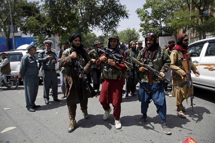 Taliban fighters patrol as two Traffic policemen stand, left, in Kabul, Afghanistan, Thursday, Aug. 19, 2021. The Taliban celebrated Afghanistan's Independence Day on Thursday by declaring they beat the United States, but challenges to their rule ranging from running a country severely short on cash and bureaucrats to potentially facing an armed opposition began to emerge. (AP Photo/Rahmat Gul)