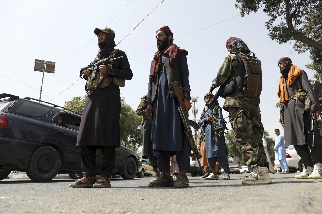 Taliban fighters patrol as two Traffic policemen stand, left, in Kabul, Afghanistan, Thursday, Aug. 19, 2021. The Taliban celebrated Afghanistan's Independence Day on Thursday by declaring they beat the United States, but challenges to their rule ranging from running a country severely short on cash and bureaucrats to potentially facing an armed opposition began to emerge. (AP Photo/Rahmat Gul)