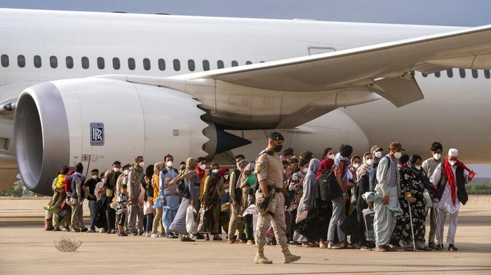 Pesawat Pengungsi Afghanistan Tiba di Spanyol Spanish health minister Carolina Darias talks to an Afghan boy after people disembarked a plane, at the Torrejon military base as part of the evacuation process in Madrid, Monday. Aug. 23, 2021. (AP Photo/Andrea Comas)
