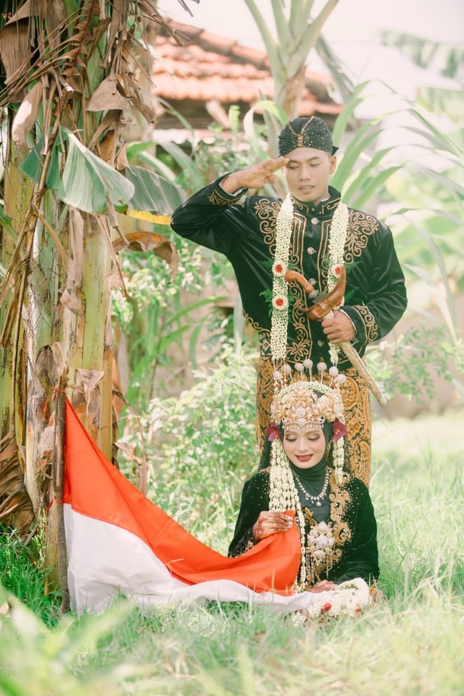 Pengantin wanita yang kini tinggal bersama dengan sang suami Anas di desa Tunjung, Kecamtan Burneh, Kabupaten Bangkalan, Madura itu menuturkan tema foto pernikahannya adalah sambil memegang bendera. Karena bertepatan dengan momen bulan Agustus hari kemerdekaan. Jadi mas Fuad mencari background alam yang natural, ini bukti bahwa kami mengambil momen foto di kebun, terang Ila. Foto: Dok. pribadi Lailatus saodah.