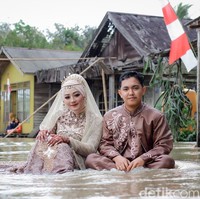 Pasangan pengantin ini viral karena foto pernikahan mereka yang tak biasa yaitu di tengah banjir. Keduanya berpose memakai busana pengantin dan berendam di air banjir. Foto: Dok/@manday_presto.