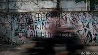 Seorang warga melintasi mural kritik sosial kepada pemerintah di salah satu sudut jalanan di Jakarta Barat, Kamis (26/8/2021).