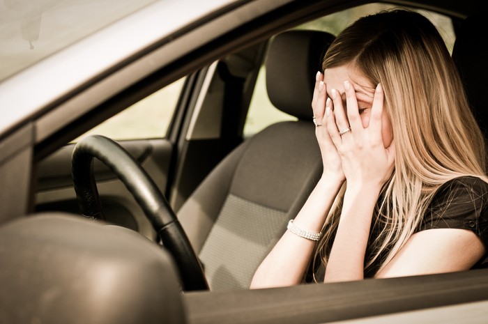491910770 Young woman with hands on eyes sitting depressed in car