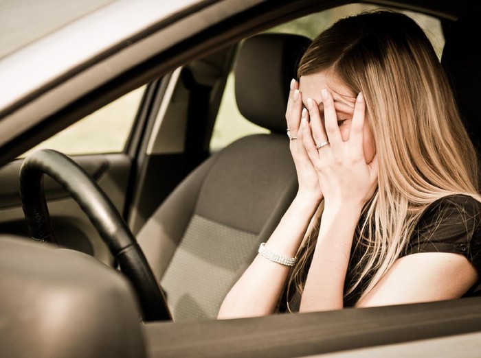 Young woman with hands on eyes sitting depressed in car