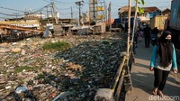 Seorang warga melintas di jembatan tersebut dengan pemandangan tumpukan sampah yang nyaris menutupi seluruh permukaan air di kali tersebut.
