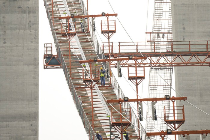 Jembatan Gantung Terpanjang di Rumania Workers install cables on the structure during a ceremony marking 100 years of diplomatic relations between Japan and Romania, at the construction site of a suspension bridge over the Danube river in Braila, Romania, Thursday, Aug. 26, 2021. The bridge, built by Japanese and Italian companies, with a span of 1,974.3 meters, will be the largest of its kind in Romania and the third in the European union.(AP Photo/Vadim Ghirda)