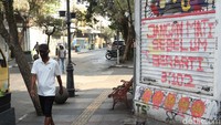 Warga melintas di depan mural bernada kritikan yang terpajang di rolling door pertokoan yang ada di Jalan Braga, Kota Bandung, Jawa Barat, Jumat (27/8).