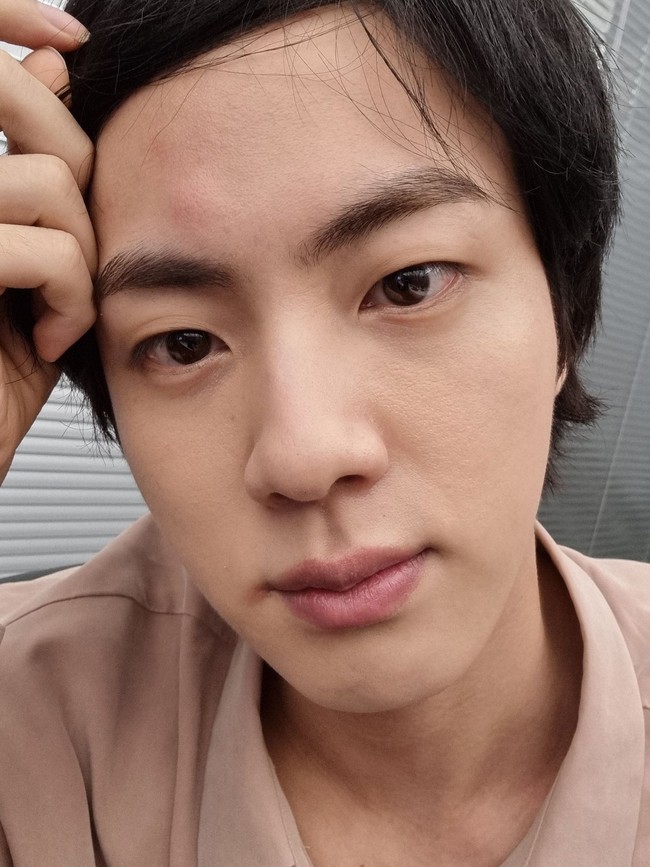 Pada Juli 2021, salah satu personel yang membagikan foto BTS tanpa makeup adalah Jin. Jin BTS berpose selfie saat tak sengaja menjedotkan kepala ke jendela hingga bengkak dan memerah. Visual grup BTS itu tetap terlihat tampan tanpa makeup. Foto: dok Weverse BTS