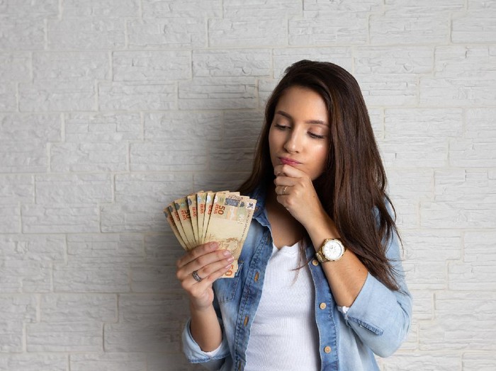 1255783831 Young pretty woman is looking at cash banknotes, Brazil Currency. Financial, profit, credit, cost, purchase, rich concept.