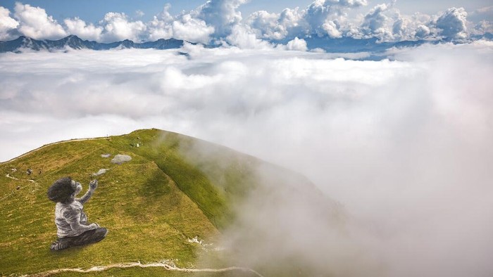 Ada Karya Seni Raksasa di Puncak Pegunungan Alpen An aerial view shows a giant landart fresco by French-Swiss artist Saype next to the Moleson summit in Moleson-sur-Gruyeres, Switzerland, Wednesday, Aug. 25, 2021. The art piece entitled 'un nouveau souffle' (a new breath) depicts a child blowing clouds towards the horizon. The Fresco covering 1500 square meters was created using biodegradable pigments made out of charcoal, chalk, water and milk proteins. (Valentin Flauraud/Keystone via AP)