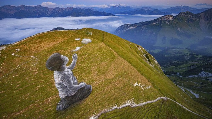 Ada Karya Seni Raksasa di Puncak Pegunungan Alpen An aerial view shows a giant landart fresco by French-Swiss artist Saype next to the Moleson summit in Moleson-sur-Gruyeres, Switzerland, Wednesday, Aug. 25, 2021. The art piece entitled 'un nouveau souffle' (a new breath) depicts a child blowing clouds towards the horizon. The Fresco covering 1500 square meters was created using biodegradable pigments made out of charcoal, chalk, water and milk proteins. (Valentin Flauraud/Keystone via AP)