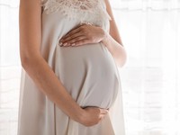 Pretty young pregnant woman standing by the window in home.