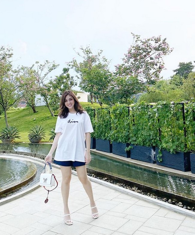 Hanya mengenakan kaos putih dan celana pendek, Dhena tetap terlihat elegan sambil menenteng tas Louis Vuitton. Foto: dok. Instagram/@dhenafrizzy