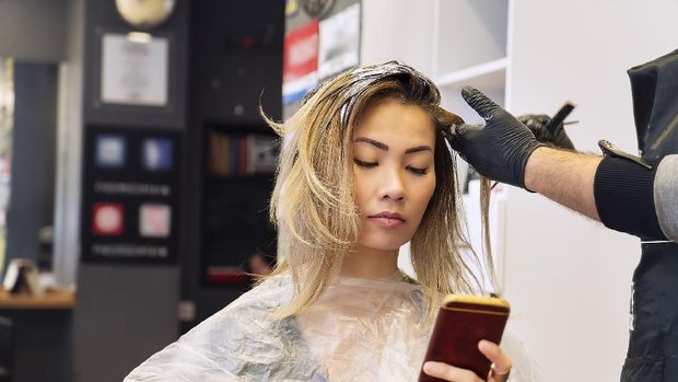 Woman on mobile phone when having hair coloring process in a hair salon