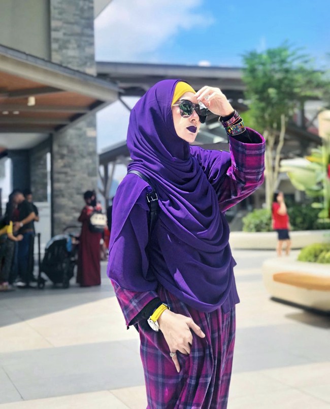 Sarah Vi membagikan foto OOTD di akun Instagramnya @sarahvi_ dengan berbagai model outfit. Tampil berbeda, Sarah memilih riasan makeup yang unik, seperti memakai warna lipstik yang senada dengan outfitnya. Dalam foto ini Sarah Vi mengaplikasikan lipstik warna ungu matte yang senada dengan khimarnya. Ia juga mengenakan tartan gamis saat berada di luar rumah. Foto: Dok. Instagram @sarahvi_.