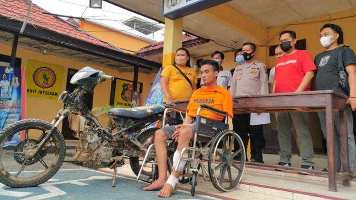 Pelaku, Anton (AN), duduk di kursi roda dengan kaki diperban.
