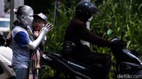 Dengan menggendong cucunya, ia berdiri di depan para pengendara yang berhenti karena lampu merah.