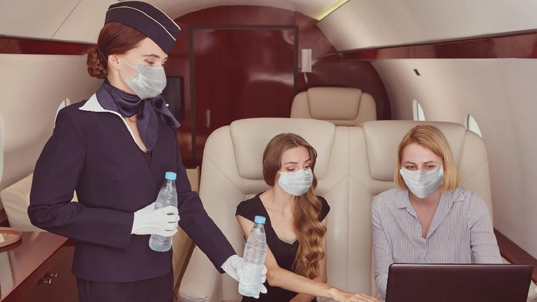 Pramugari Air hostess in medical protective mask from coronavirus covid-19 pandemic inside airplane is serving passengers in the first class.