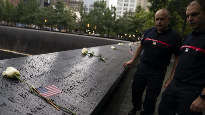 Visitors browse the south pool as flowers and American flags rest among the names of the fallen at the National September 11 Memorial & Museum, Thursday, Sept. 9, 2021, in New York. (AP Photo/John Minchillo)