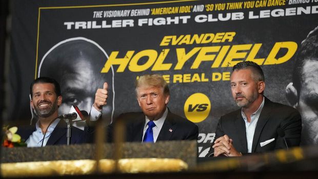 Former President Donald Trump, center, gives a thumbs-up to cheering supporters as he and his son Donald Trump Jr., left, prepare to provide commentary for a boxing event headlined by a bout between former heavyweight champ Evander Holyfield and former MMA star Vitor Belfort, Saturday, Sept. 11, 2021, in Hollywood, Fla. (AP Photo/Rebecca Blackwell)