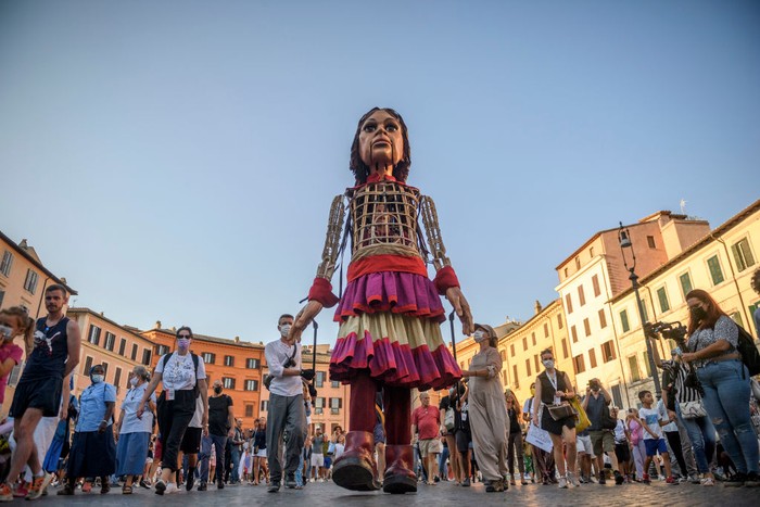 Boneka Raksasa Little Amal saat Keliling Italia ROME, ITALY - SEPTEMBER 12: People greet Little Amal, a giant puppet depicting a young Syrian refugee girl, as she walks in the city, on September 12, 2021 in Rome, Italy. Little Amal is a 3.5 meter puppet walking 8,000 kilometers across Europe to highlight the plight of child refugees. There are some 26 million refugees worldwide, and more than half of them are children. (Photo by Antonio Masiello/Getty Images)