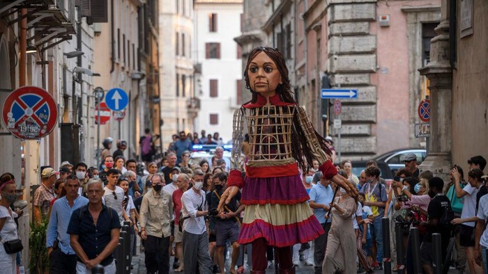 ROME, ITALY - SEPTEMBER 12: People greet Little Amal, a giant puppet depicting a young Syrian refugee girl, as she walks in the city, on September 12, 2021 in Rome, Italy. Little Amal is a 3.5 meter puppet walking 8,000 kilometers across Europe to highlight the plight of child refugees. There are some 26 million refugees worldwide, and more than half of them are children. (Photo by Antonio Masiello/Getty Images)