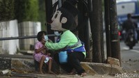 Sementara suaminya berprofesi sebagai pemulung keliling. Menjadi pengamen berkostum dilakukan guna mencukupi biaya keluarga dan menyekolahkan anak.