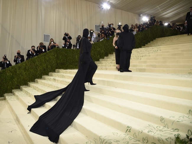 Kehadiran Kim Kardashian di Met Gala 2021 bersama seorang pria yang juga berbaju hitam hingga seluruh wajahnya tertutup sempat membuatnya dikira rujuk dengan Kanye West. Namun sosok pria tersebut bukanlah Kanye, melainkan creative director Balenciaga Demna Gvasalia. Foto: Evan Agostini/Invision/AP