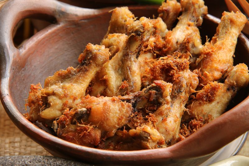 ayam goreng Fried chicken, the common main side dish for many Indonesian rice dishes, such as Nasi Uduk Betawi. The chicken has been cooked using traditional recipe hence it brings the grind galangal and lemongrass as the tasty, crispy crumbs scattering around the chicken. Chicken drummettes have been used for aesthetics reason. The drummettes are plated on an traditional earthenware wok.