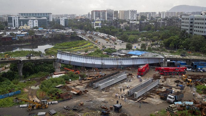 Workers stand near an under-construction bridge that collapsed in Mumbai, India, Friday, Sept. 17, 2021. According to police more than a dozen people were injured after a part of the under-construction bridge collapsed early Friday morning in Mumbai. (AP Photo/Rafiq Maqbool)