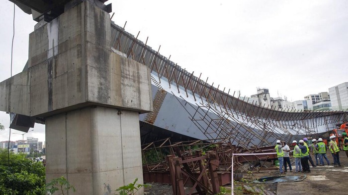 Workers stand near an under-construction bridge that collapsed in Mumbai, India, Friday, Sept. 17, 2021. According to police more than a dozen people were injured after a part of the under-construction bridge collapsed early Friday morning in Mumbai. (AP Photo/Rafiq Maqbool)