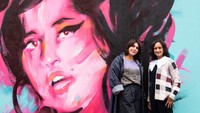 Kurator pameran Priya Khanchandani dan Naomi Parry berpose di depan mural Amy Winehouse. Foto: Getty Images/Jeff Spicer