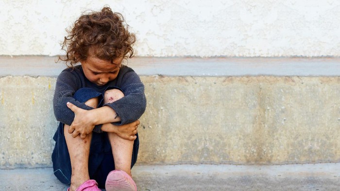 poor, sad little child girl sitting against the concrete wall