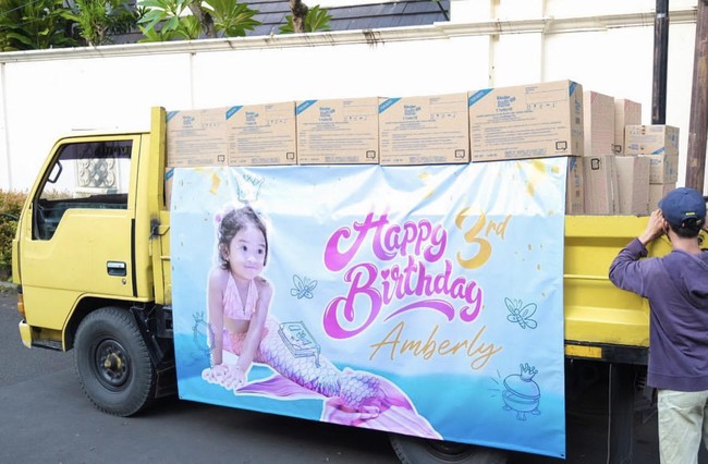 Di depan truk tersebut terdapat spanduk ucapan Happy birthday Amberly yang memakai kostum putri duyung. Acara tersebut diadakan di kolam renang kediaman Shandy dan Gilang. Tema acara ulang tahun pun diberi tema Kinder Joy Pool Party. Dan didekorasi dengan balon warna lilac dan snowblue. Foto: Dok.Instagram @juragan99.