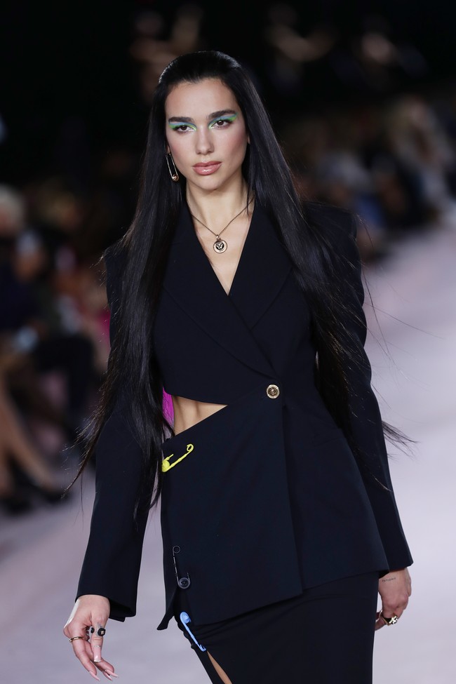 Di catwalk, Dua Lipa menebar pesonanya dalam balutan blazer dengan detail cut-out nan seksi di bagian pinggang dan rok pensil senada. Tak ketinggalan safety pins khas Versace turut menghiasi busana tersebut. (Foto: Getty Images/Vittorio Zunino Celotto)