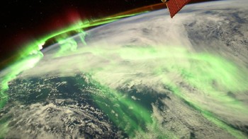 Penampakan spektakuler aurora seakan menyelimuti Bumi, dari titik 240 kilometer di atas sana memperlihatkan cahaya hijau aurora tinggi di atmosfer sementara di kejauhan, ada sinar kemerahan. Sedangkan di bawahnya adalah area awan-awan yang berarak di atas lautan. ESA/Thomas Pesquet