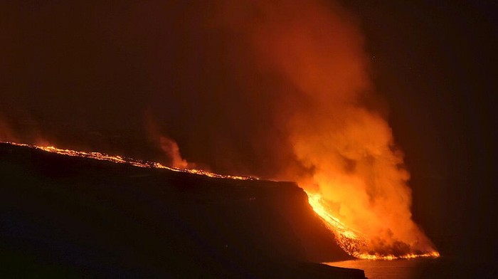 In this photo made available by Ume (Unidad Militar de Emergencias), Military Emergency Unit personal take gas reading measurements near a volcano on the Canary island of La Palma, Spain, in the early hours of Tuesday Sept. 28, 2021. Lava flowing from an erupting volcano on the Spanish island of La Palma has picked up pace on its way to the sea. Officials say it is now within about 800 meters (875 yards) of the shoreline. When the molten rock eventually meets the sea water it could trigger explosions and toxic gas. (Luismi Ortiz/UME via AP)