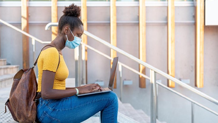 beautiful and young black girl who studies and works with a laptop around the city, blogger and smart worker in times of epidemic surf the internet, use multimedia content, use of protective mask in times of epidemic