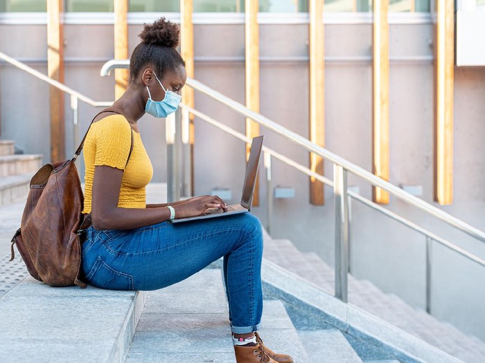 beautiful and young black girl who studies and works with a laptop around the city, blogger and smart worker in times of epidemic surf the internet, use multimedia content, use of protective mask in times of epidemic