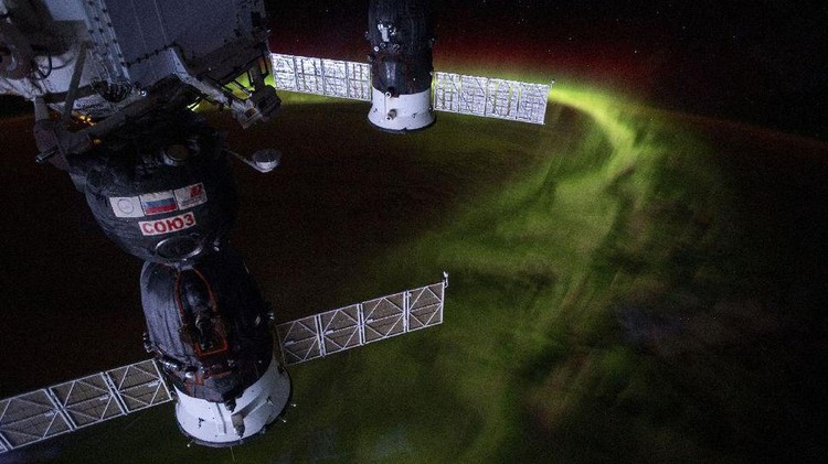 Penampakan spektakuler aurora seakan menyelimuti Bumi, dari titik 240 kilometer di atas sana memperlihatkan cahaya hijau aurora tinggi di atmosfer sementara di kejauhan, ada sinar kemerahan. Sedangkan di bawahnya adalah area awan-awan yang berarak di atas lautan.