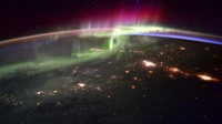 Penampakan spektakuler aurora seakan menyelimuti Bumi, dari titik 240 kilometer di atas sana memperlihatkan cahaya hijau aurora tinggi di atmosfer sementara di kejauhan, ada sinar kemerahan. Sedangkan di bawahnya adalah area awan-awan yang berarak di atas lautan.